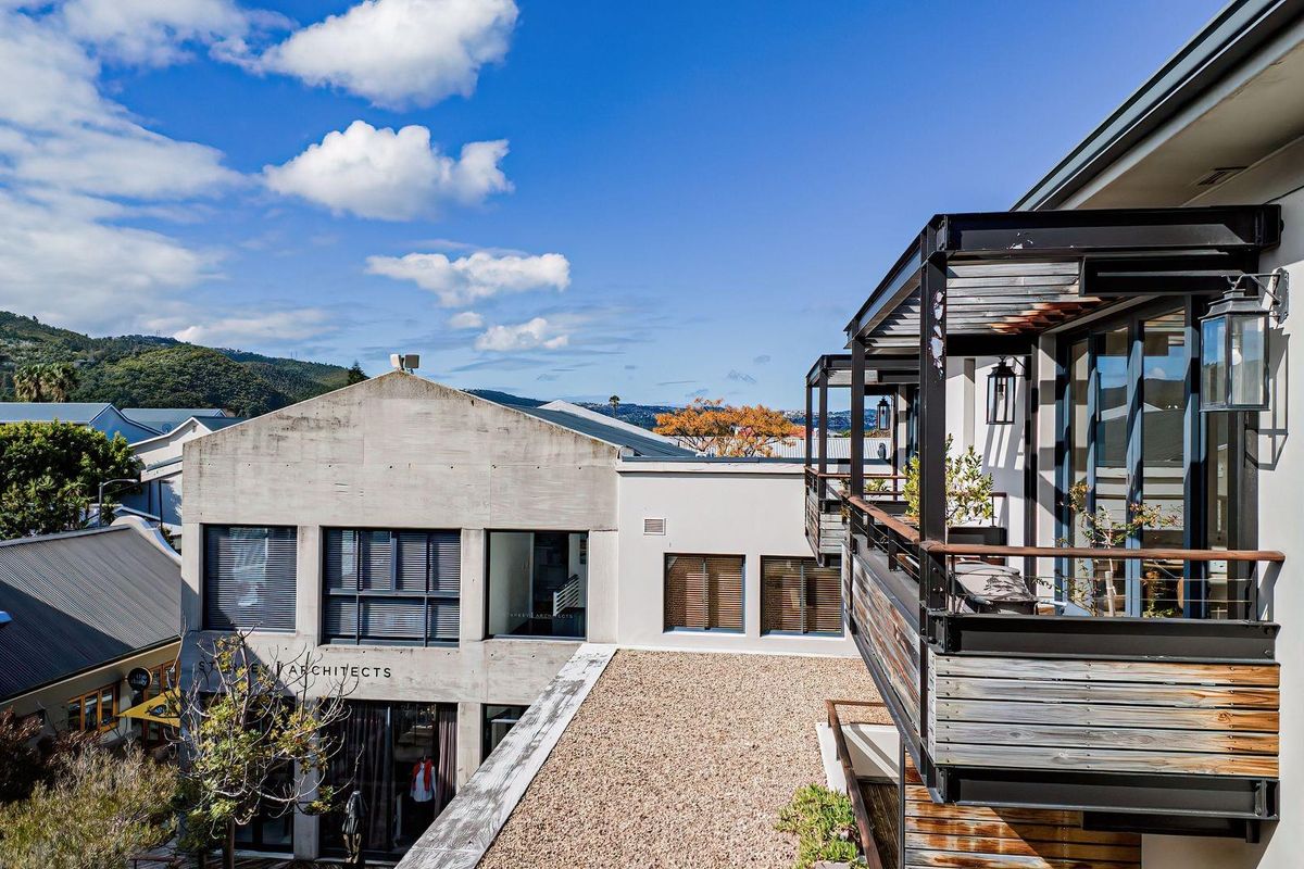 An elevated view of a modern apartment building featuring a steel-framed balcony with timber decking and a gravel-covered roof terrace.