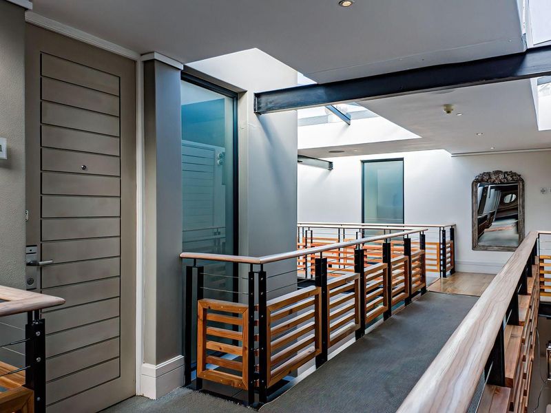 A modern, well-lit apartment hallway featuring a timber and steel balustrade, exposed structural steel beams, and multiple skylights providing natural light.