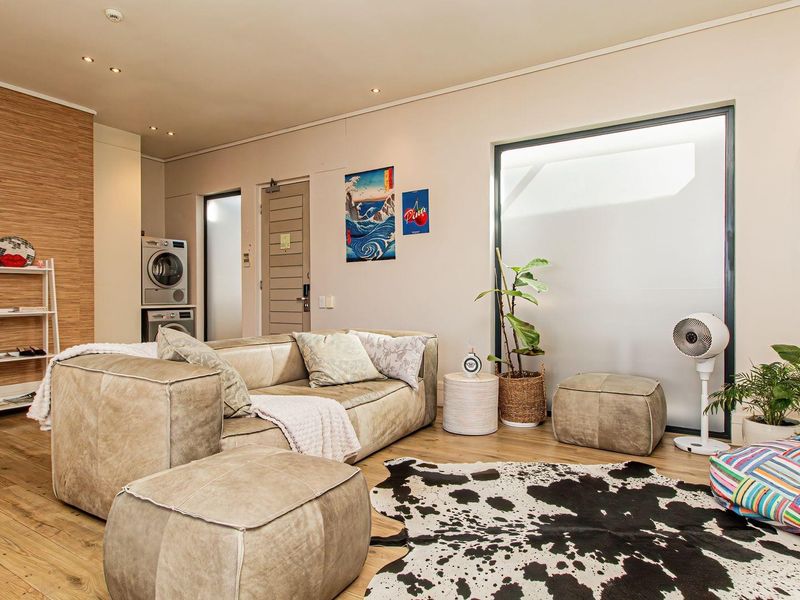 A modern living area featuring timber flooring, recessed lighting, and a discreet built-in laundry space with integrated appliances.