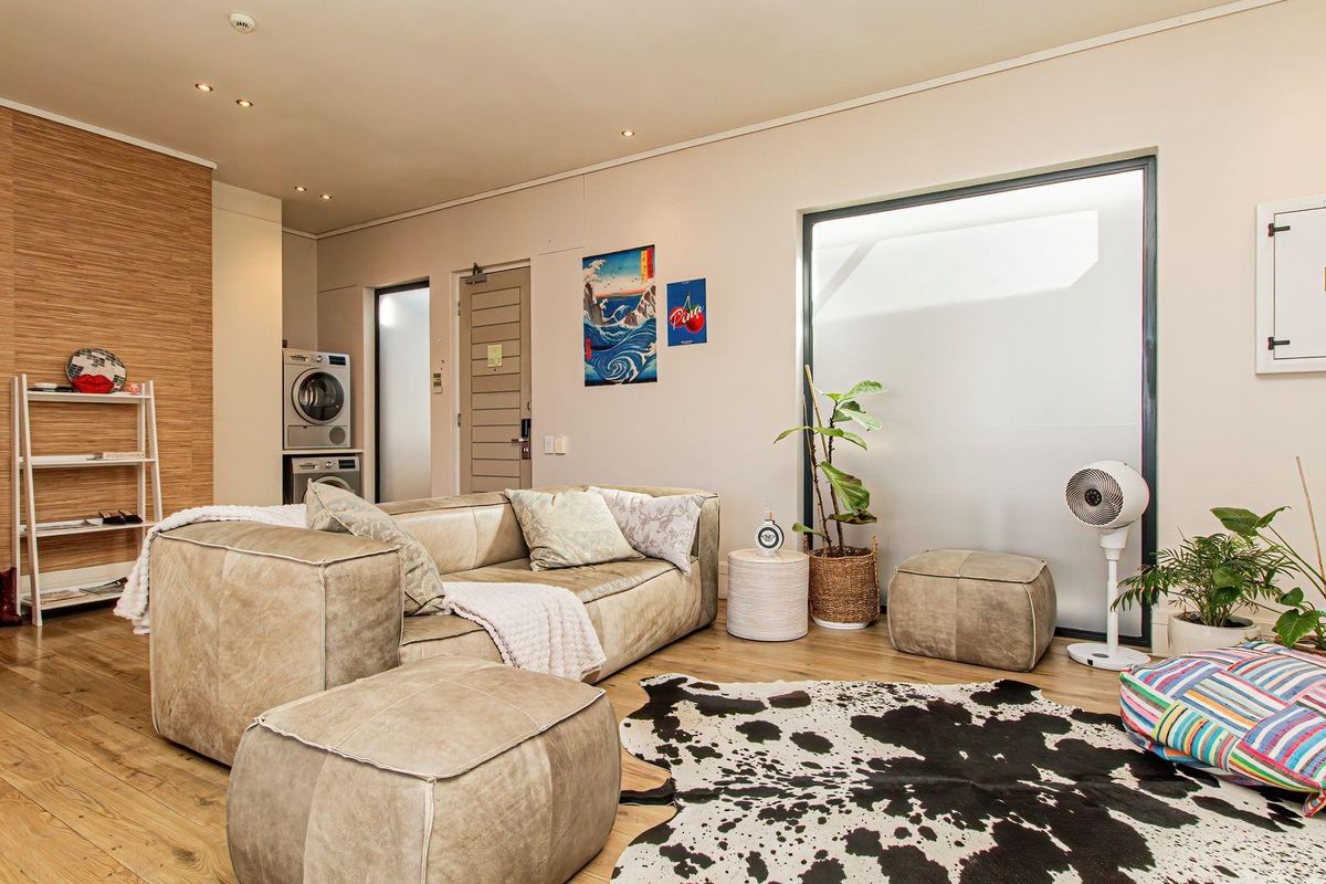 A modern living area featuring timber flooring, recessed lighting, and a discreet built-in laundry space with integrated appliances.