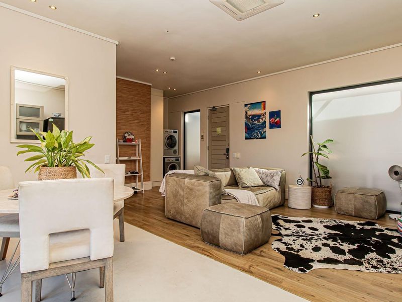 An open-plan living and dining area featuring laminate flooring, recessed lighting, and a discreet built-in laundry space.