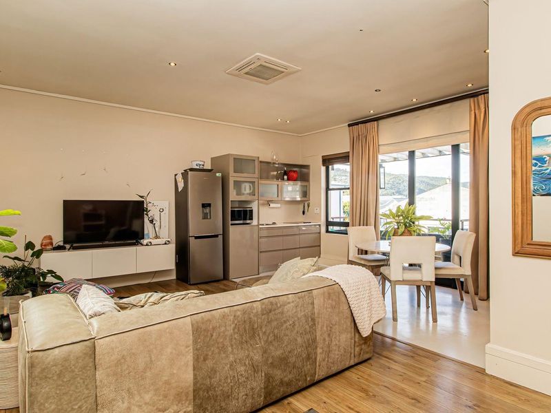 An open-plan living and dining area featuring laminate flooring, recessed lighting, a ceiling-mounted air conditioner, and direct access to a balcony through sliding doors.