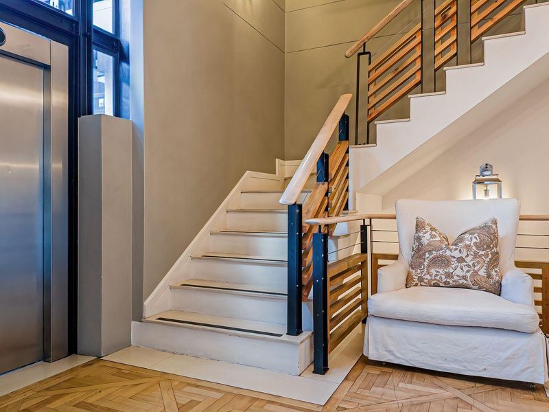 A modern apartment entrance foyer featuring a stainless steel elevator, elegant timber staircase with matching handrails, and high-quality parquet flooring.