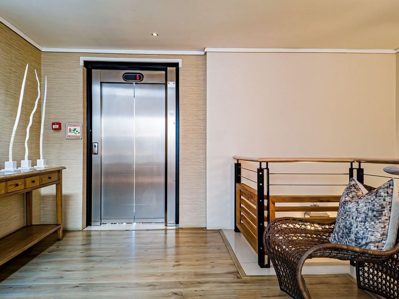 A well-maintained apartment hallway featuring a modern stainless steel elevator, timber flooring, and a contemporary timber and metal balustrade.
