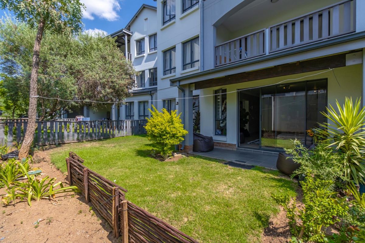 Rear view of the townhouse featuring a private garden, tiled patio area, and upper-level balcony with timber railings.