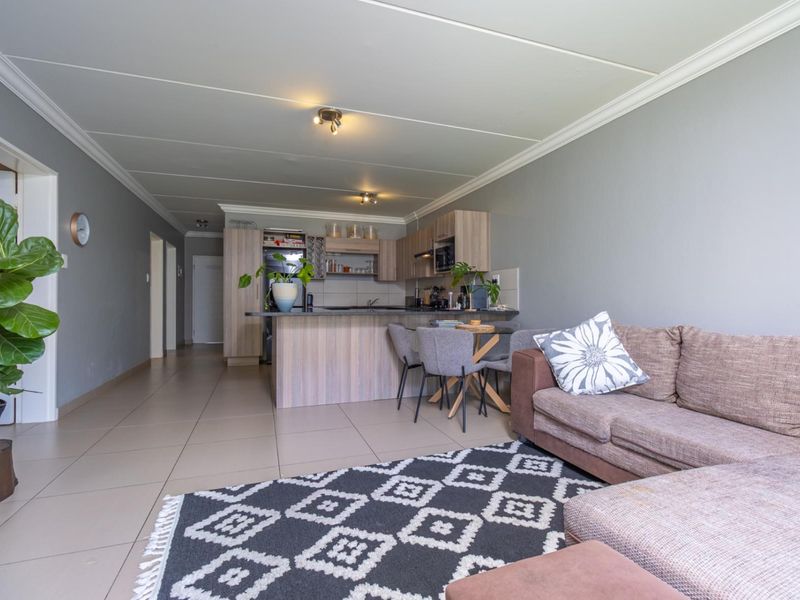 Open-plan living area featuring a modern kitchen with built-in cabinetry and island, seamlessly flowing into the lounge space with neutral tiled flooring.