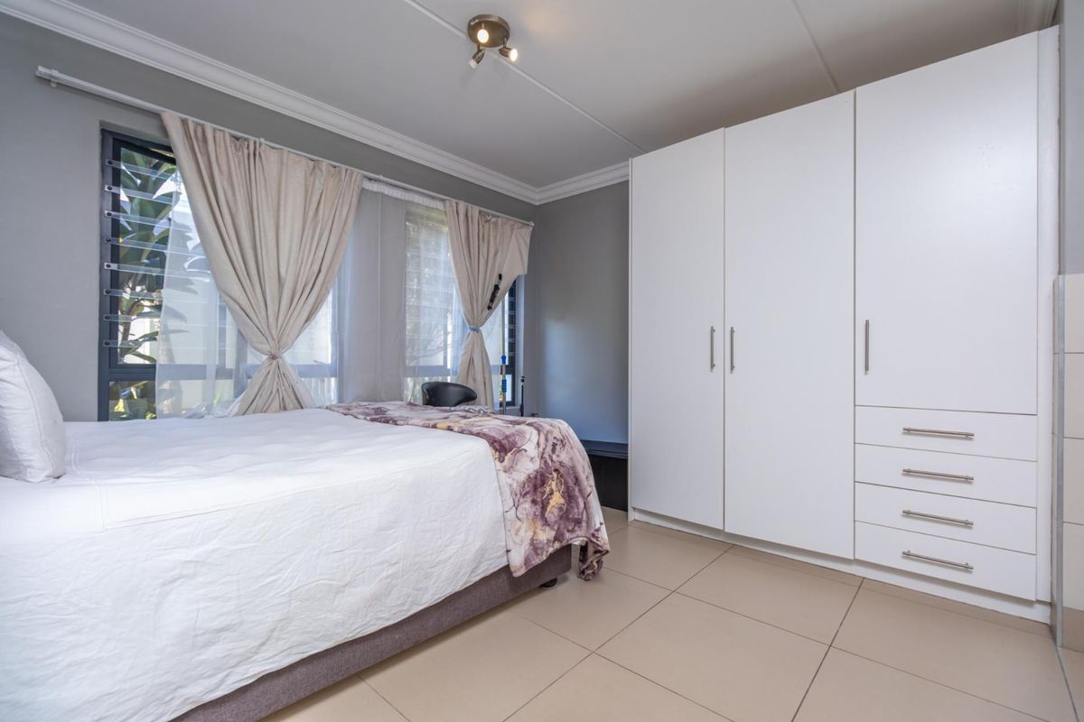 A well-maintained bedroom featuring neutral tiled flooring, built-in white cupboards, and louver windows that allow for natural light and ventilation.