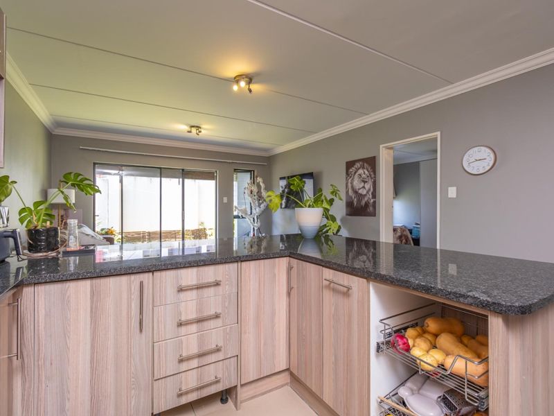Open plan kitchen featuring granite countertops, light wood-finish cabinetry, and integrated storage, flowing seamlessly into the adjacent living area with access to the patio.