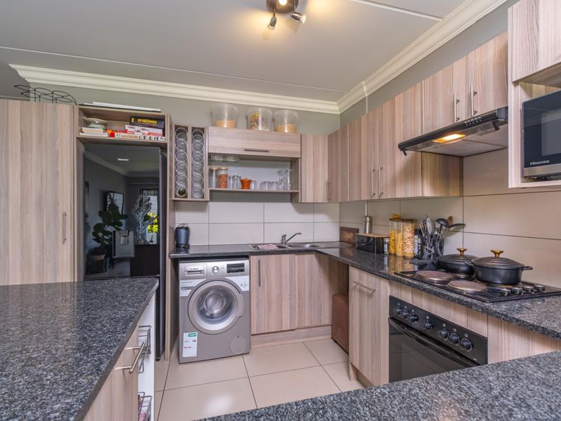 A functional kitchen featuring granite countertops, built-in oven with hob, extractor fan, and integrated cabinetry with a tiled splashback and flooring.