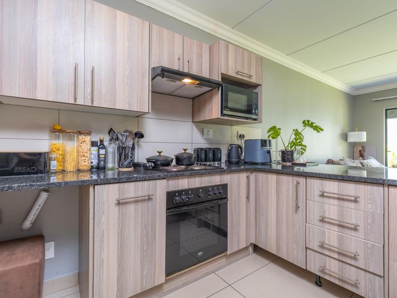 A functional kitchen featuring wood-look laminate cabinetry, granite countertops, built-in oven, extractor fan, and tiled flooring.