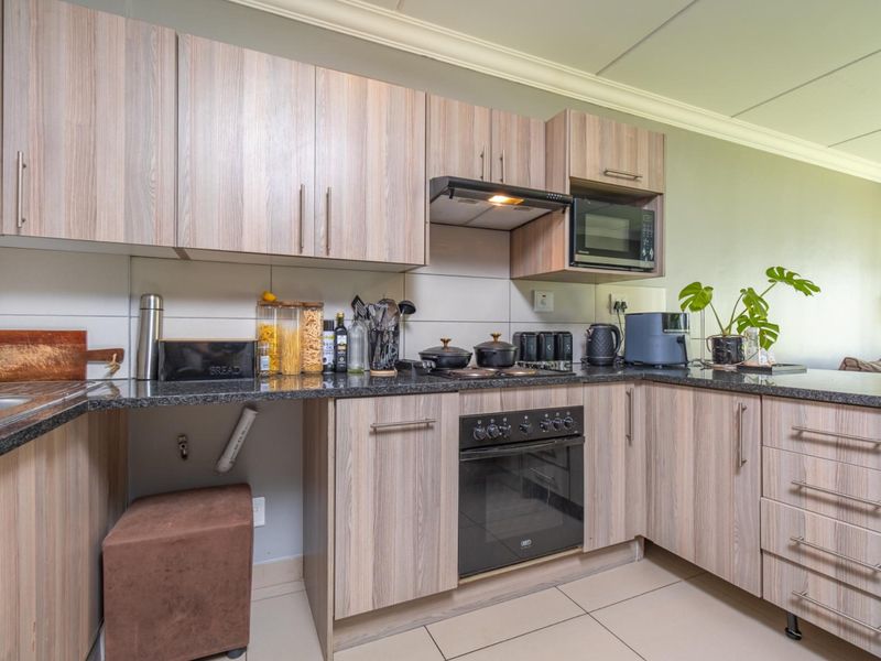 A functional kitchen featuring wood-look laminate cabinetry, granite countertops, built-in oven, and extractor fan, with tiled flooring and backsplash.