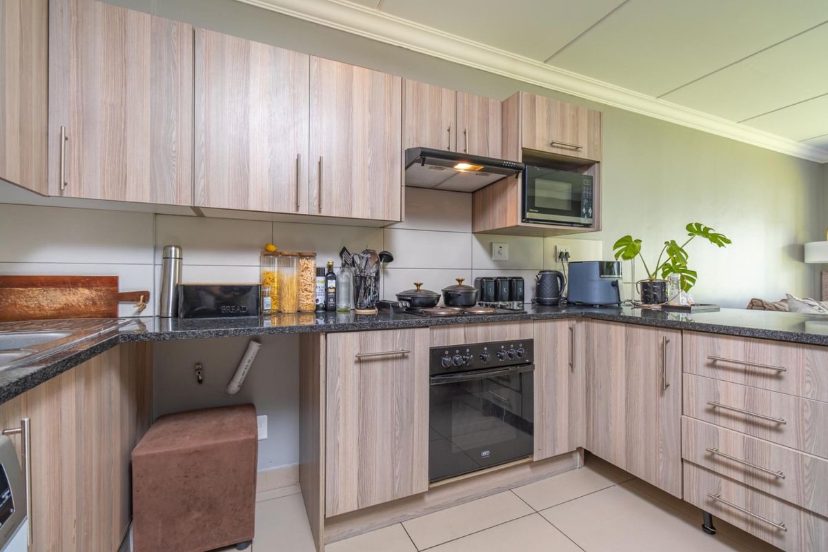 A functional kitchen featuring wood-look laminate cabinetry, granite countertops, built-in oven, and extractor fan, with tiled flooring and backsplash.