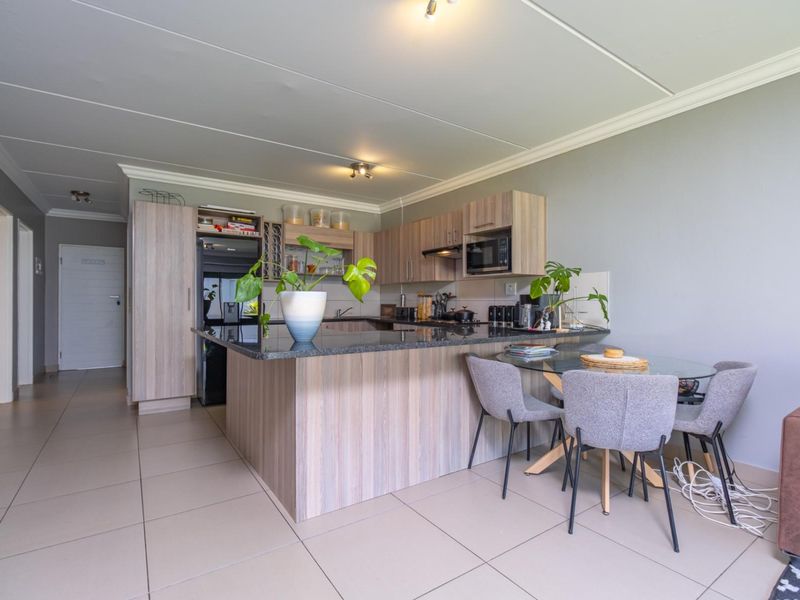 Open-plan kitchen featuring modern laminate cabinetry, granite countertops, and integrated appliances, seamlessly flowing into the dining area with neutral ceramic floor tiles.