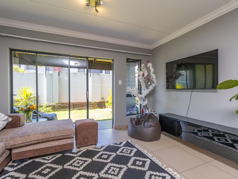 A bright living room featuring tiled flooring, coved ceilings, and large sliding glass doors providing direct access to the rear patio and garden area.
