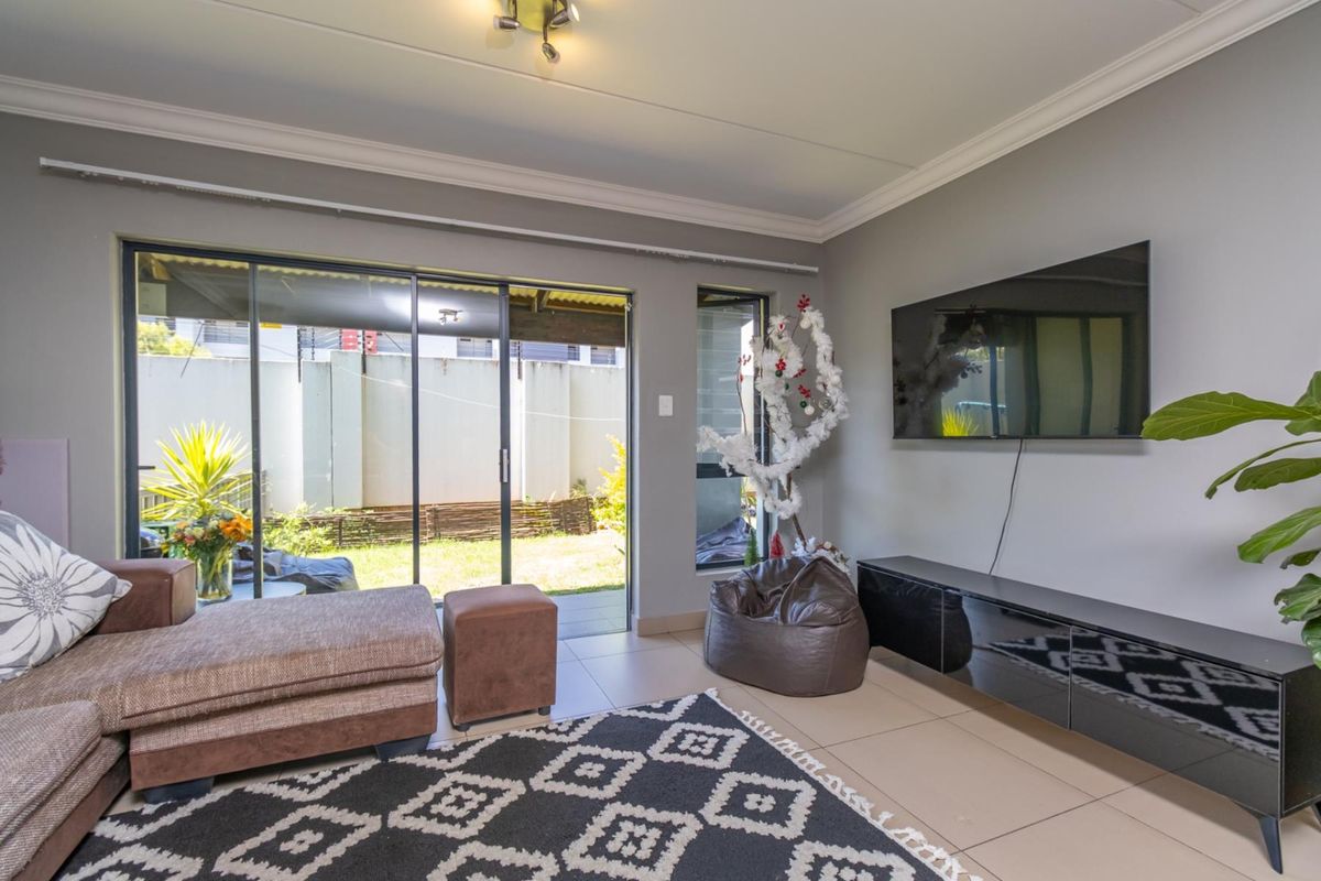 A bright living room featuring tiled flooring, coved ceilings, and large sliding glass doors providing direct access to the rear patio and garden area.