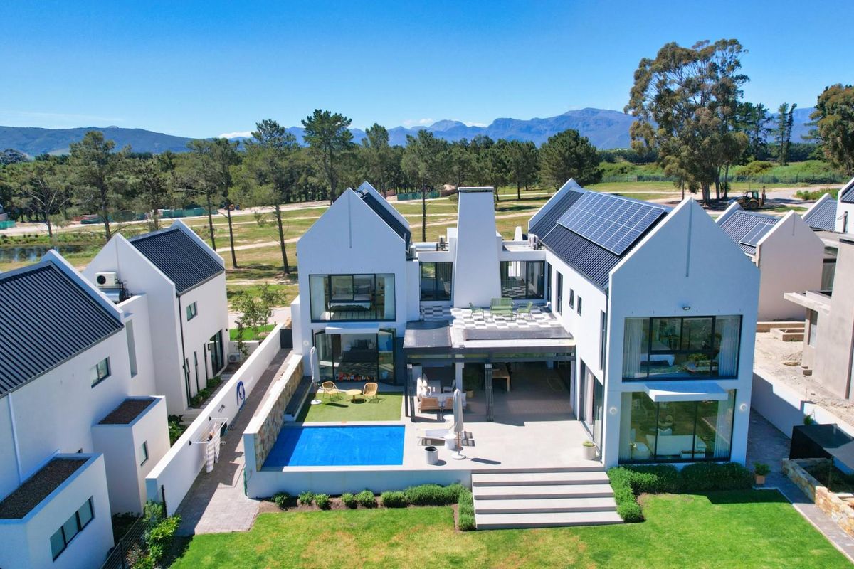 Aerial view of a modern luxury residence featuring a swimming pool, covered patio, and solar panel installation set within a landscaped estate.
