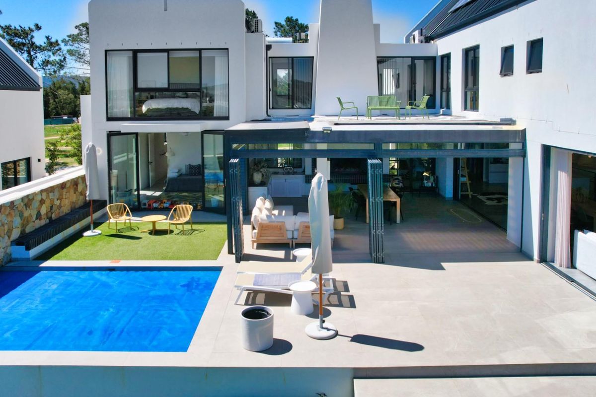 Modern rear exterior featuring a swimming pool, covered patio area, stone-clad retaining wall, and an upper-level balcony with large glass sliding doors.