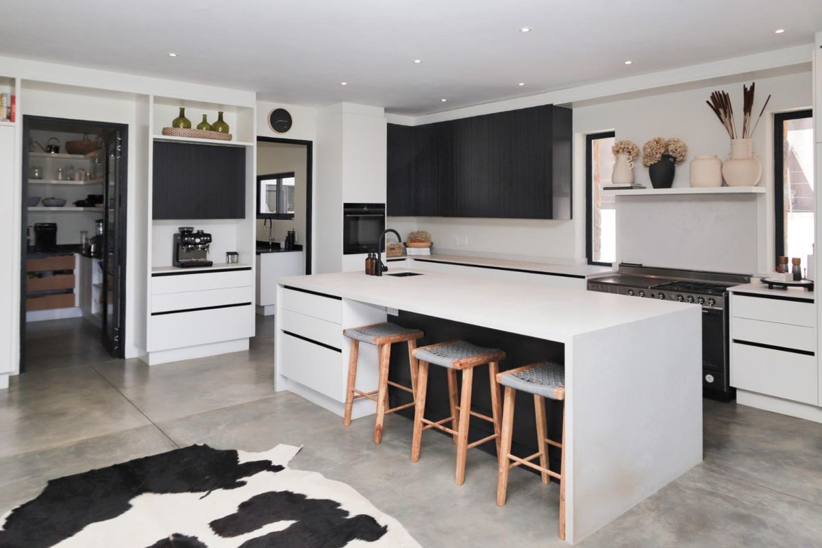 Modern kitchen featuring a large central island, sleek cabinetry, built-in appliances, and polished concrete flooring, with an adjacent scullery area.