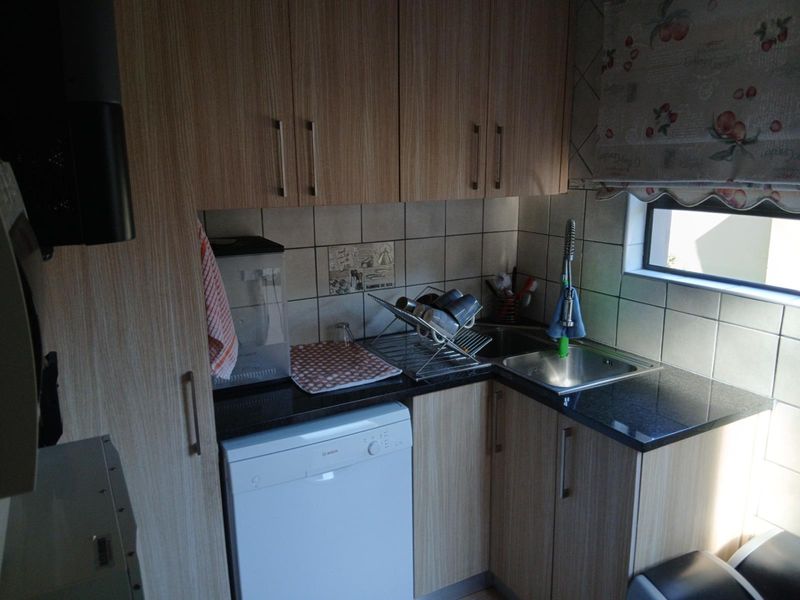 Compact scullery area featuring laminate cabinetry, granite countertops, a stainless steel sink, and an integrated dishwasher.