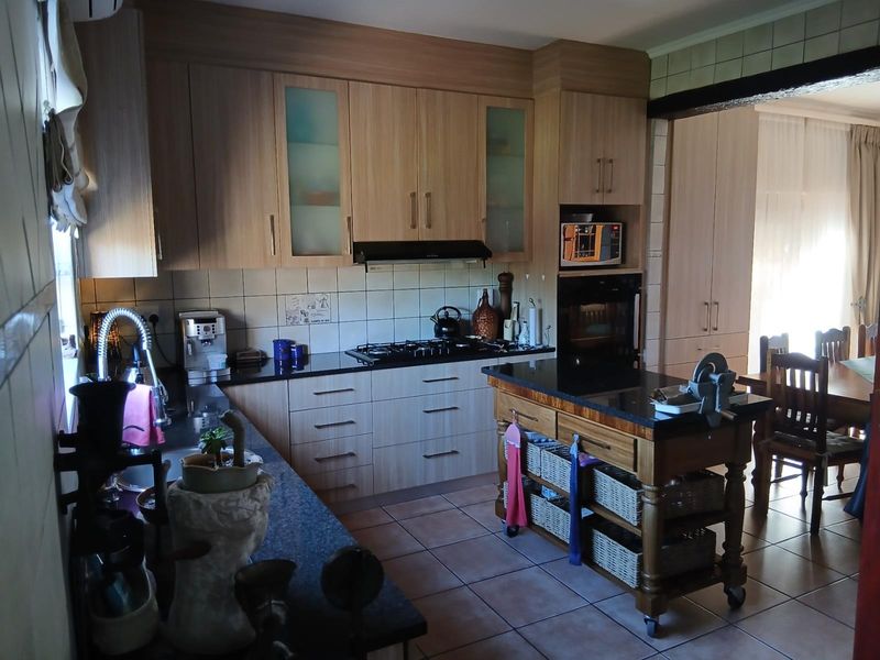 A functional kitchen featuring light wood cabinetry, granite countertops, a gas hob, built-in oven, and tiled flooring, with an integrated island unit.
