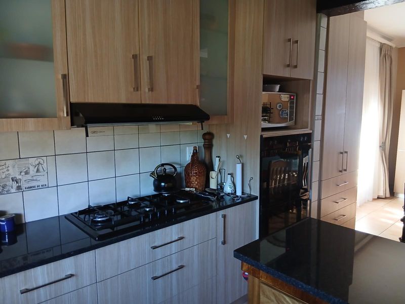 Modern kitchen featuring light wood cabinetry, black granite countertops, a gas hob with extractor fan, and a built-in oven.