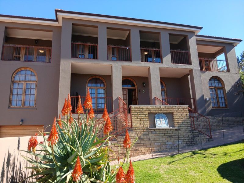 A well-maintained double-storey house featuring a prominent brick staircase, arched timber-framed windows, and an expansive upper-level balcony with metal railings.