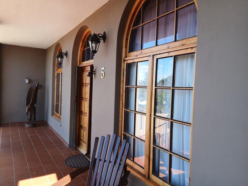 A covered patio area featuring terracotta tiling, arched timber-framed windows, and a classic arched entrance door with wall-mounted lighting.