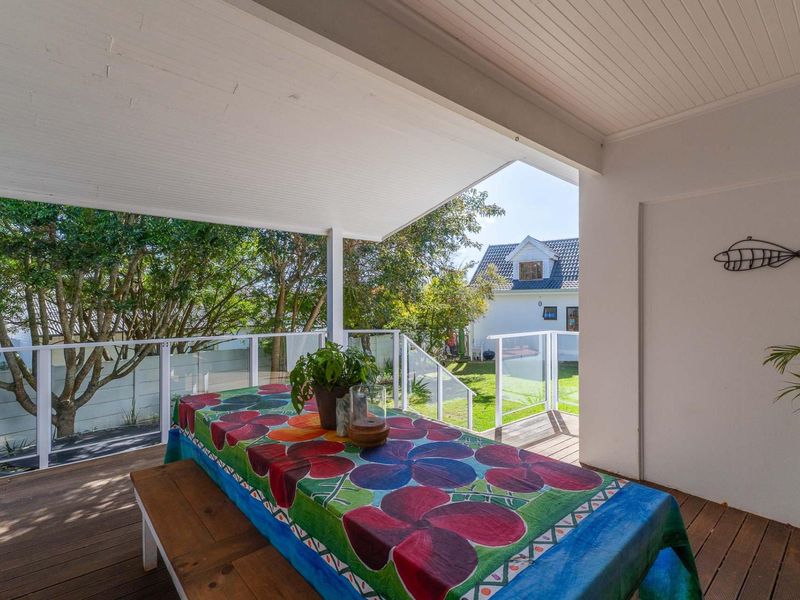 A covered outdoor patio featuring timber decking and a modern glass balustrade, overlooking a private garden area.