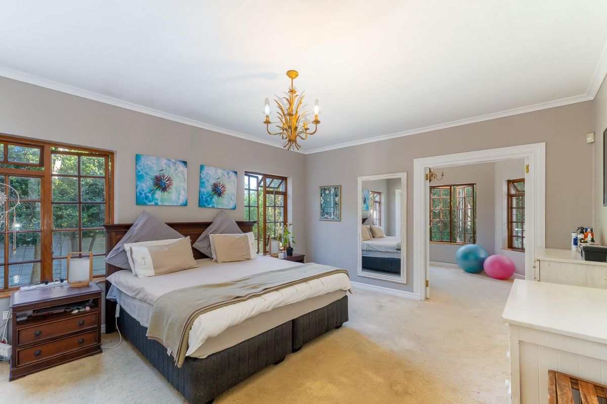 Spacious bedroom featuring timber-framed windows, neutral wall tones, and a classic chandelier, with an adjoining room visible through the doorway.