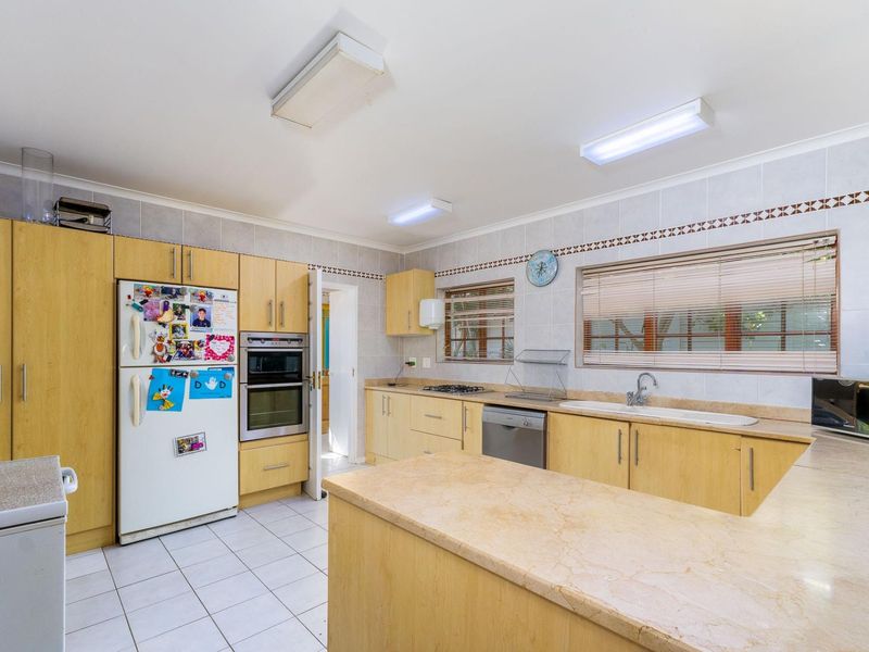 A functional kitchen featuring light wood cabinetry, a double oven, gas hob, double sink, and tiled flooring with ample counter space.