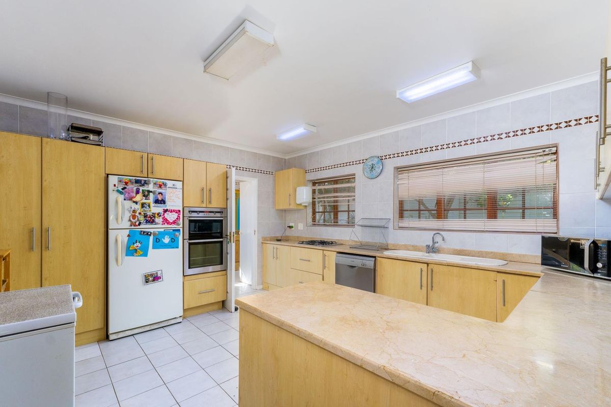 A functional kitchen featuring light wood cabinetry, a double oven, gas hob, double sink, and tiled flooring with ample counter space.