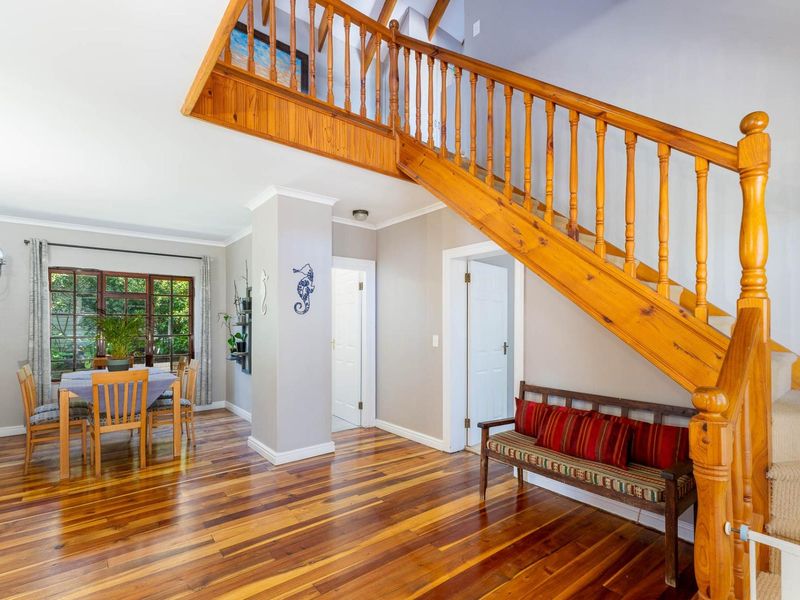 Welcoming entrance hall featuring polished hardwood flooring and a prominent timber staircase leading to the upper level, adjacent to a dining area.