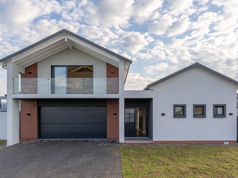 Modern two-story residential facade featuring a gabled roof, brick accents, a glass-railed balcony, and a paved driveway leading to a double garage.