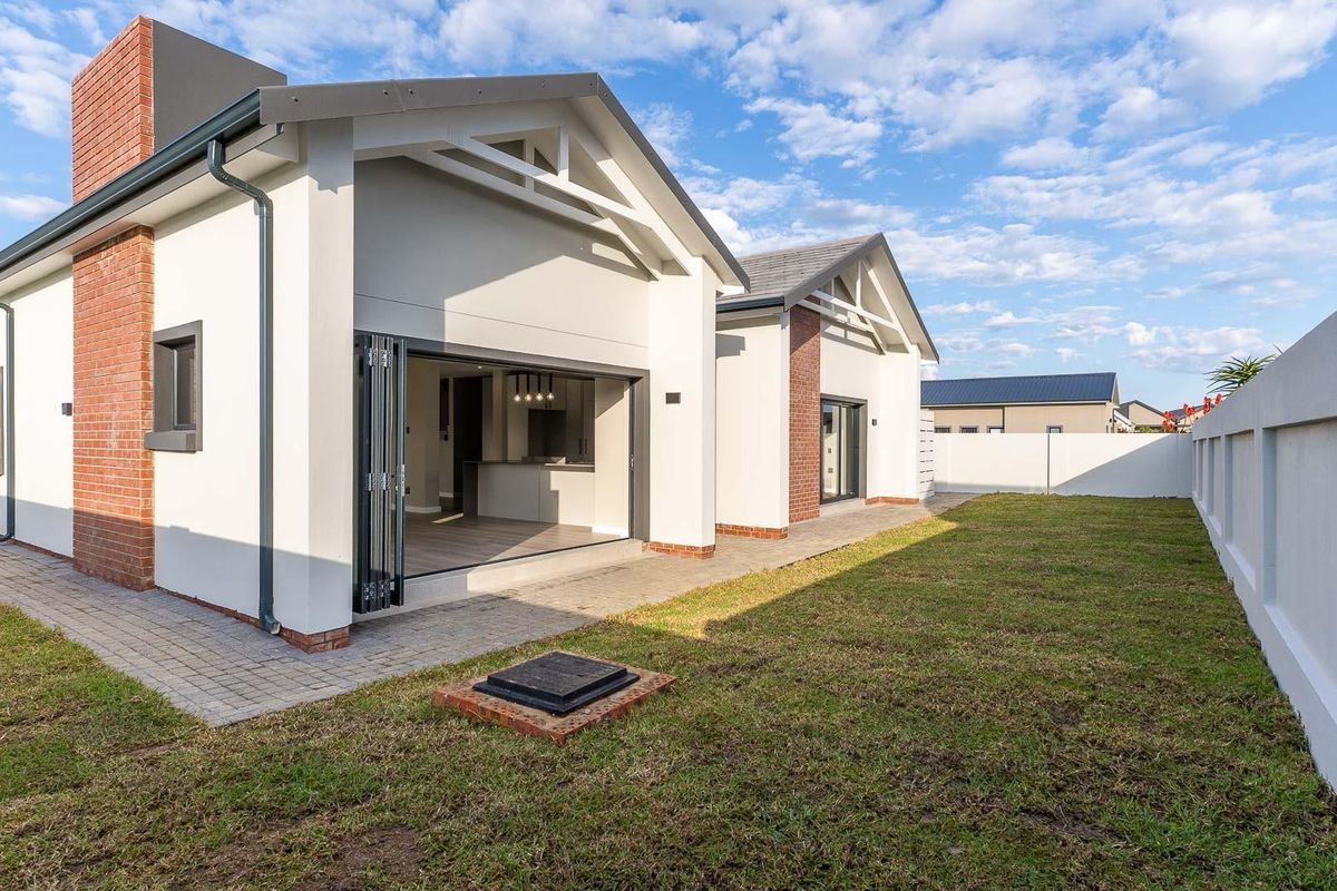 Rear view of a modern house featuring a paved patio, bi-fold doors leading to the interior, and a private garden with a boundary wall.