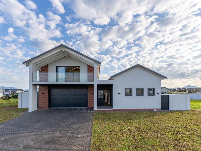 Modern double-story residential home featuring a paved driveway, double garage, and a glass-fronted balcony under a gabled roof structure.