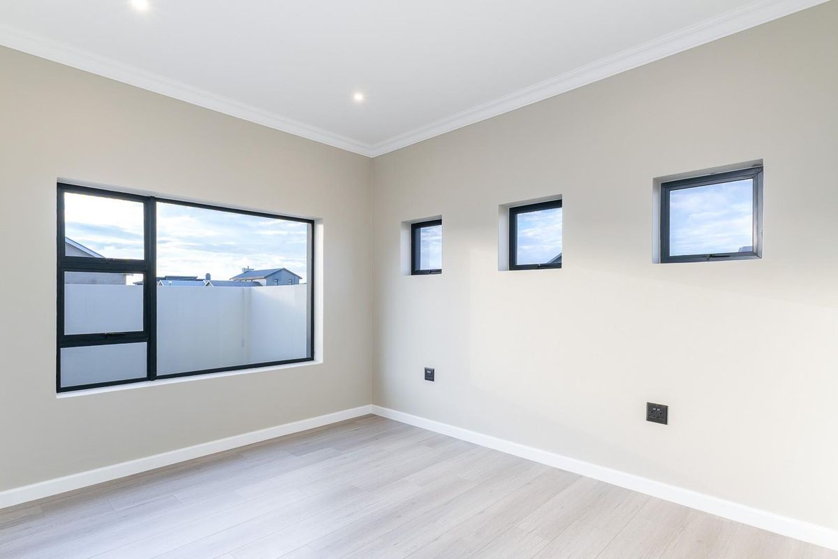 A bright, modern, and empty bedroom featuring neutral walls, laminate flooring, recessed lighting, and contemporary aluminium-framed windows.