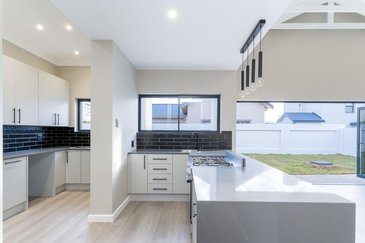 Modern kitchen featuring sleek cabinetry, stone countertops, gas hob, and subway tile backsplash, with seamless flow to the outdoor area through stacking doors.
