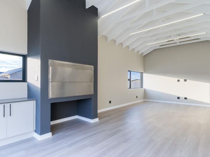 Spacious living area featuring a vaulted ceiling with exposed rafters, built-in fireplace, and modern laminate flooring in a clean, contemporary setting.