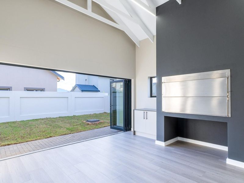 Spacious living area featuring a vaulted ceiling with exposed trusses, built-in braai, and large stacking doors opening to the rear garden.