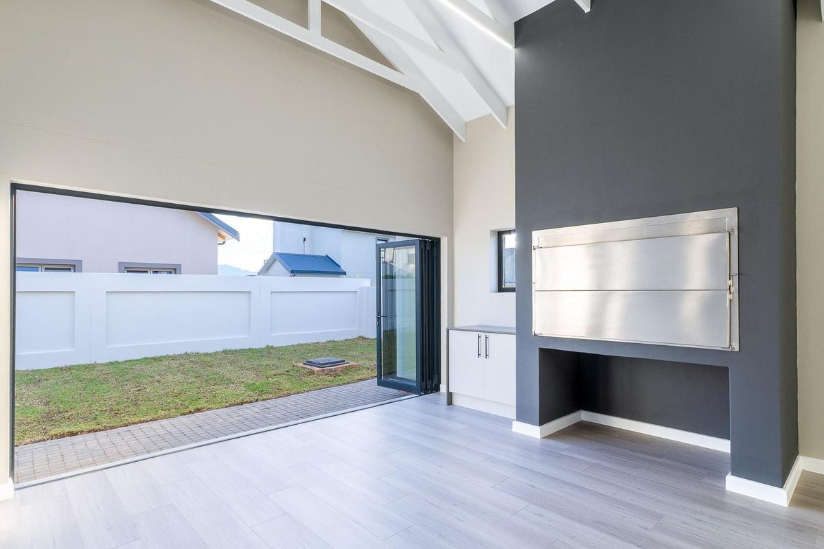Spacious living area featuring a vaulted ceiling with exposed trusses, built-in braai, and large stacking doors opening to the rear garden.