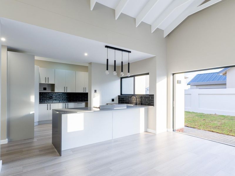 Modern open-plan kitchen featuring a central island, sleek cabinetry, black tile backsplash, and vaulted ceilings with direct access to the rear garden.