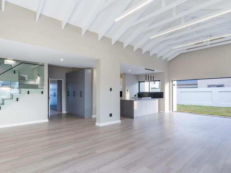 Spacious open-plan living area featuring vaulted ceilings with exposed rafters, modern kitchen with island, and a sleek staircase with glass balustrades.