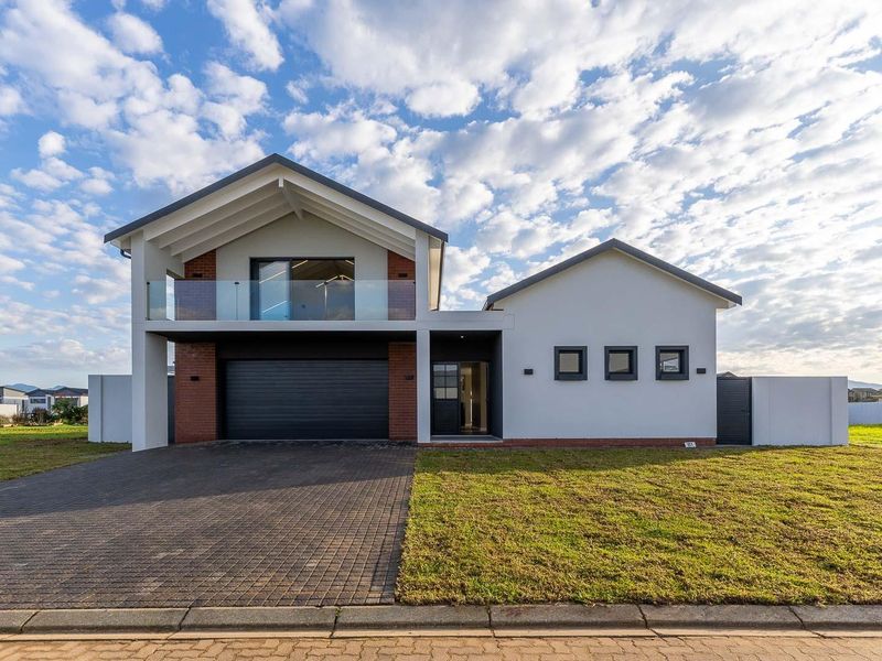 Modern double-story residential home featuring a paved driveway, integrated double garage, and a glass-fronted upper balcony.