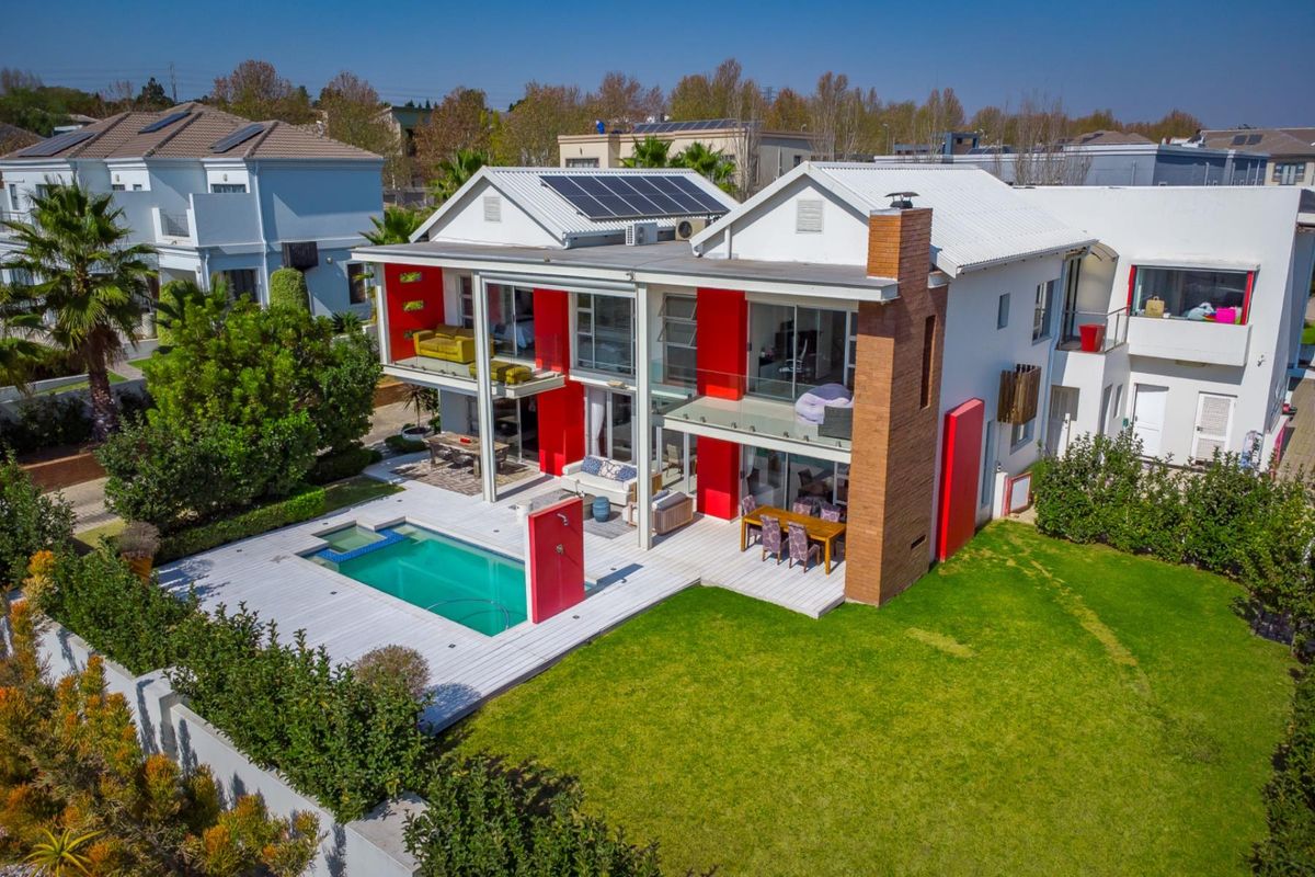 Aerial view of the rear exterior featuring a swimming pool, wooden decking, solar panels, and a modern two-story facade with glass balconies.