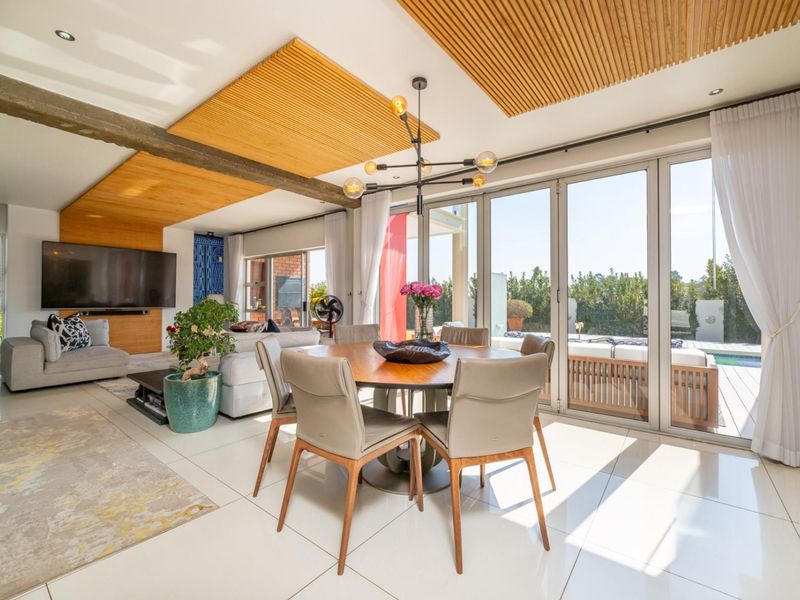 Spacious open-plan living and dining area featuring a timber slat ceiling detail, exposed beam, and large stacking doors opening to the pool deck.