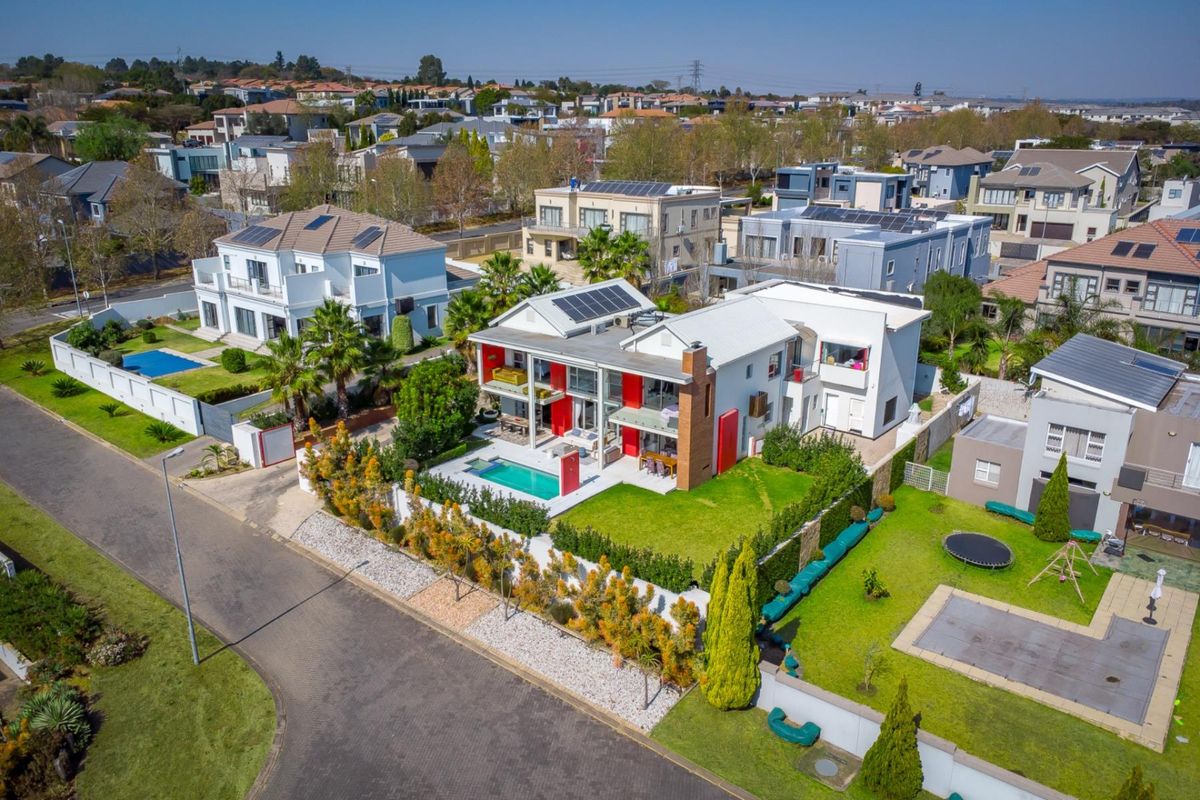 Aerial view of a modern residential property featuring a swimming pool, solar panels, and a well-maintained garden in a suburban estate setting.