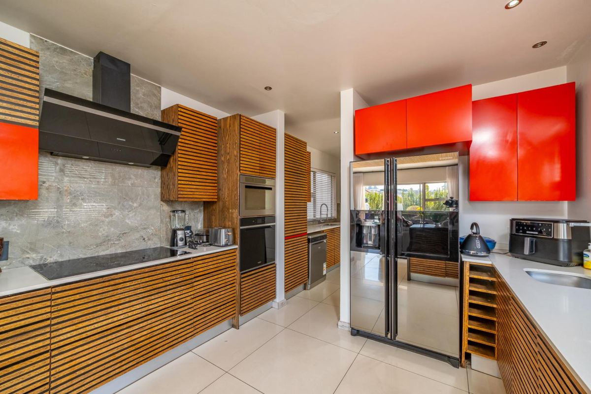 Modern kitchen featuring a striking contrast between slatted wood and vibrant red cabinetry, stone-look backsplash, and high-end built-in appliances.
