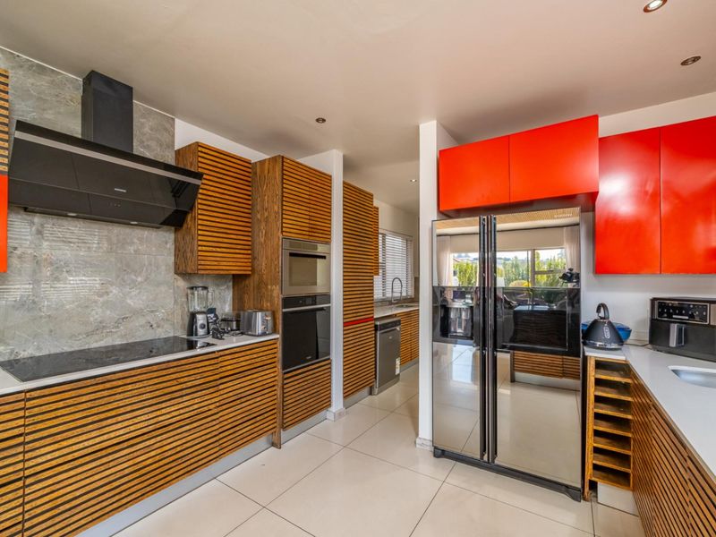 Modern kitchen featuring a striking contrast between slatted wood and vibrant red cabinetry, stone-look backsplash, and high-end built-in appliances.
