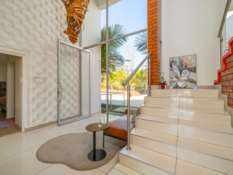 Grand entrance foyer featuring a striking textured feature wall, exposed brickwork, a tiled staircase with stainless steel railing, and expansive floor-to-ceiling glass windows.