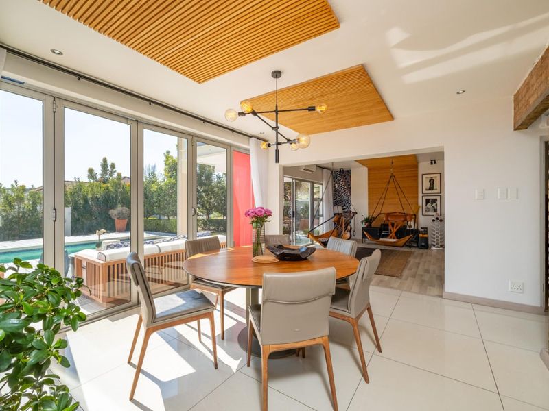 Bright open-plan dining area featuring timber slat ceiling accents, large bi-fold doors opening to the pool area, and a striking exposed brick feature wall.
